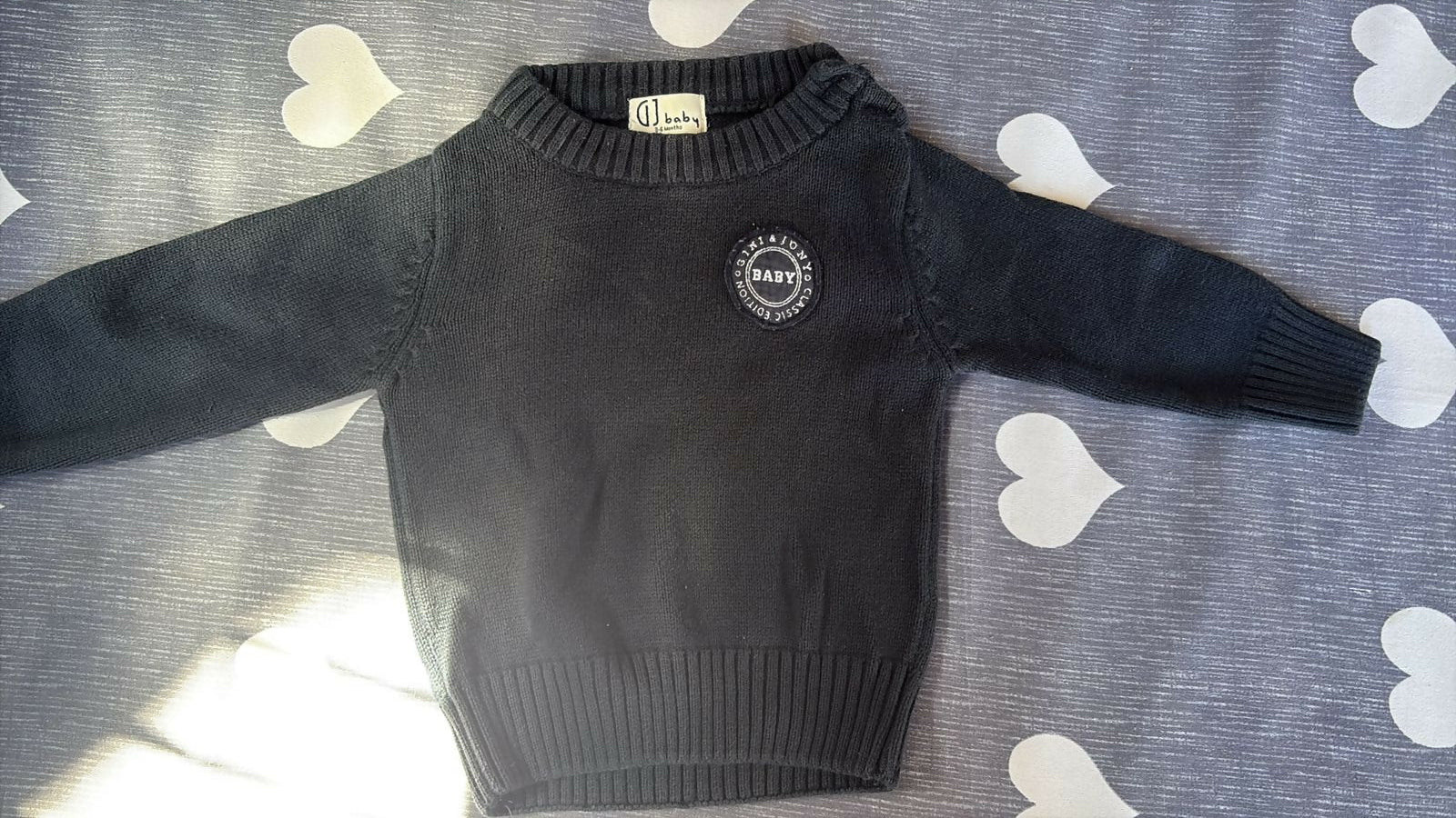 Black sweater with a logo on a gray surface with heart patterns