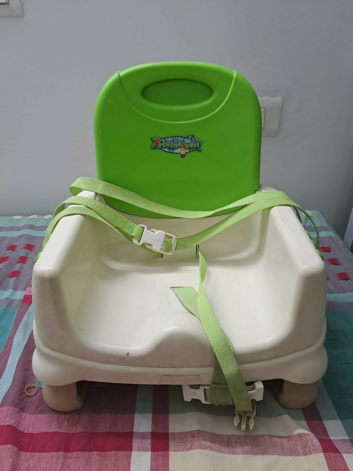 Green and white baby booster seat on a checkered tablecloth