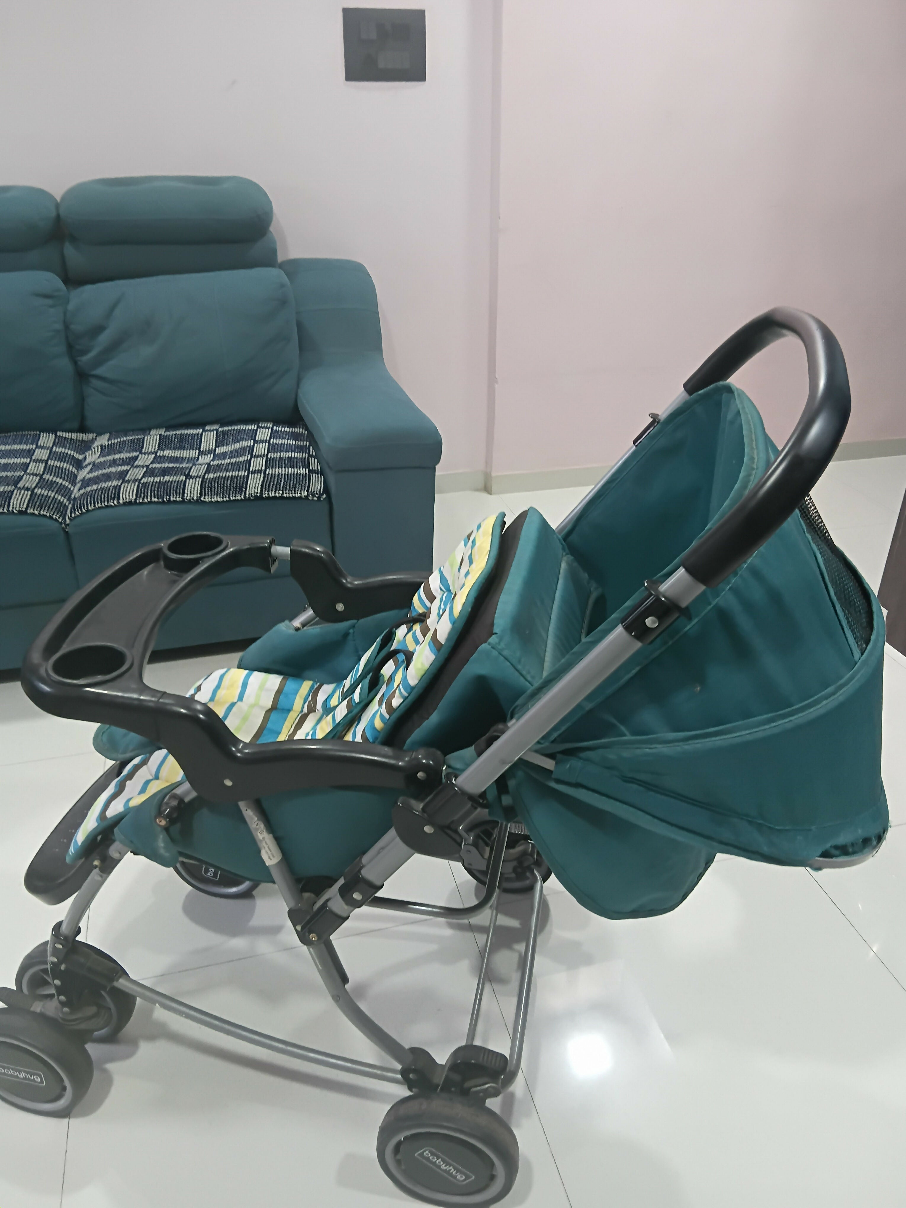 Teal stroller with a patterned seat cover in a living room setting.