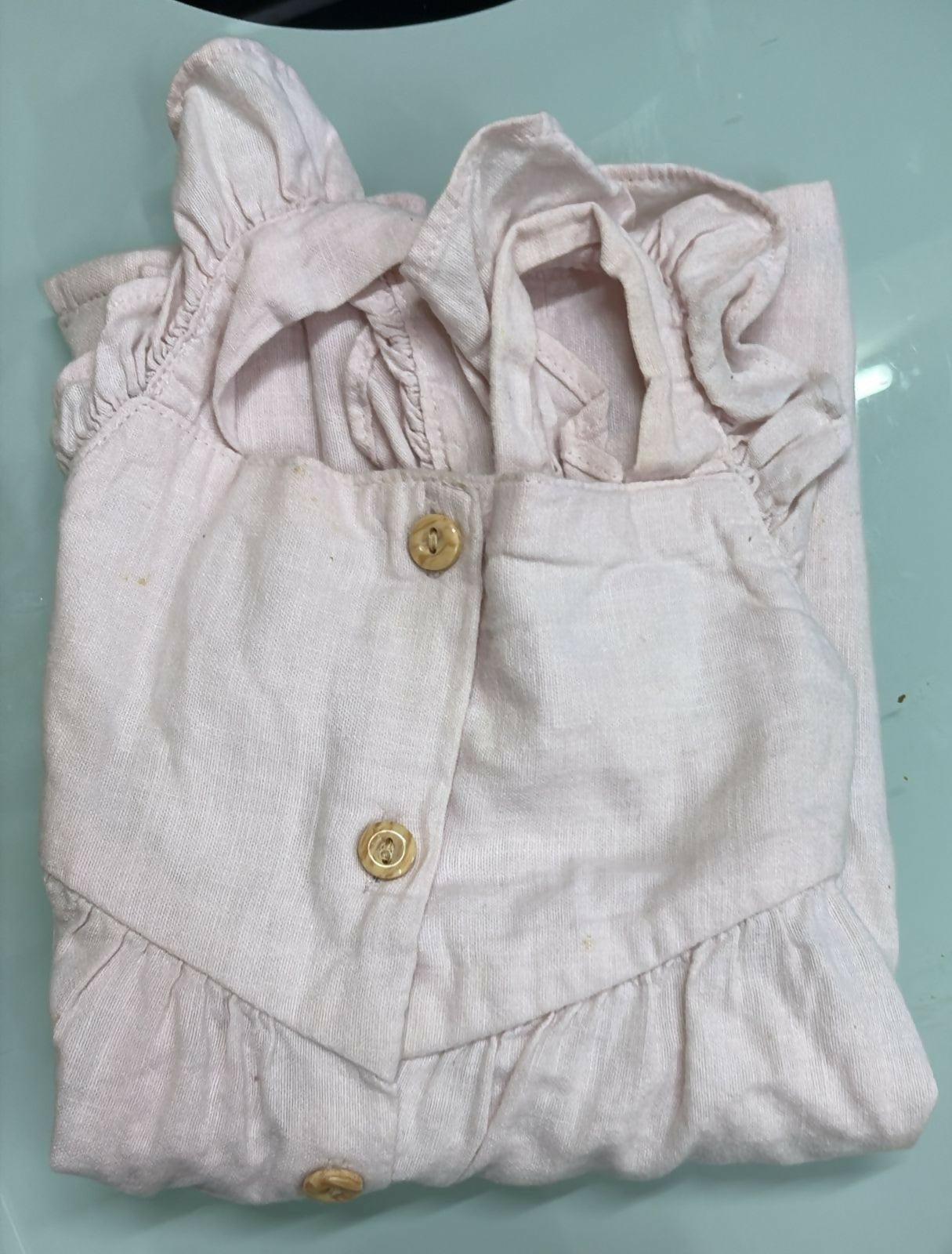 Folded light pink baby outfit with ruffled details on a light blue surface