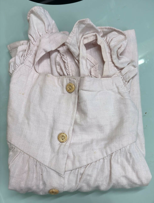 Folded light pink baby outfit with ruffled details on a light blue surface