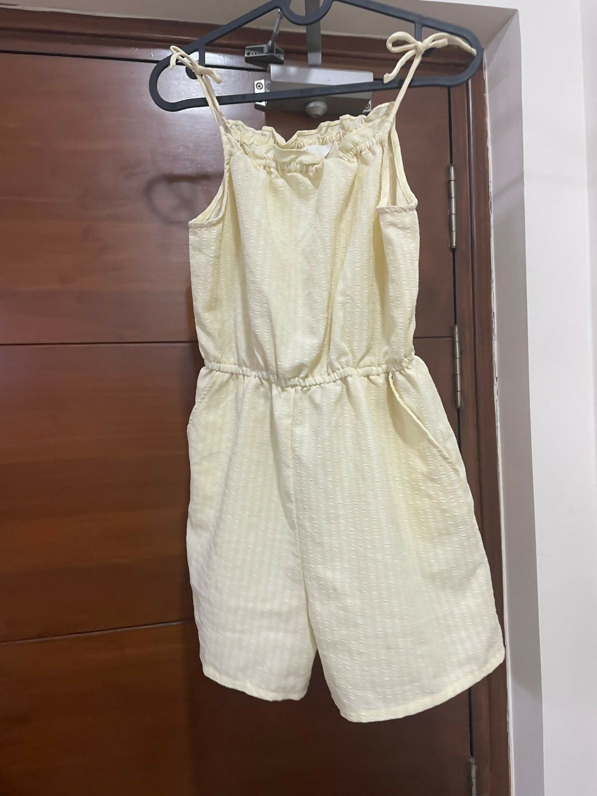 Light yellow romper hanging on a wooden door