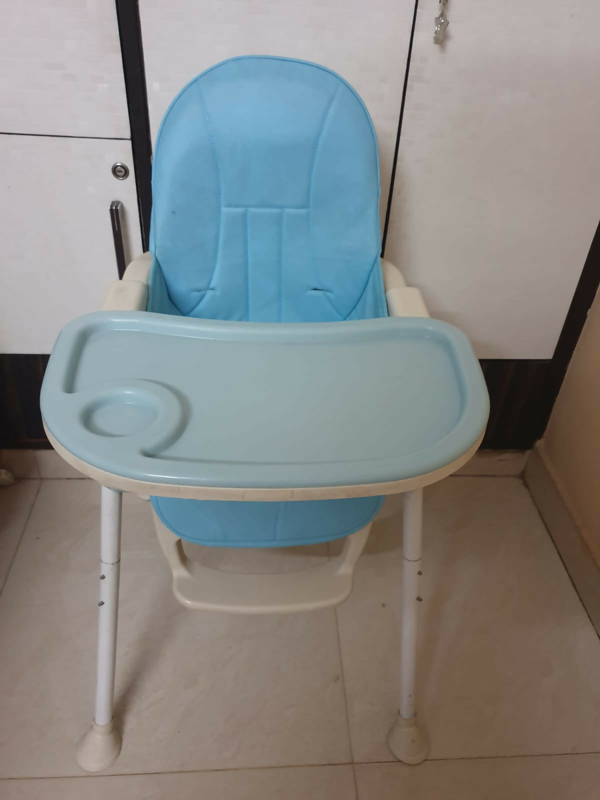 Blue baby high chair with white legs on a tiled floor.