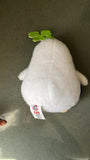 White plush toy with a green leaf on a gray surface