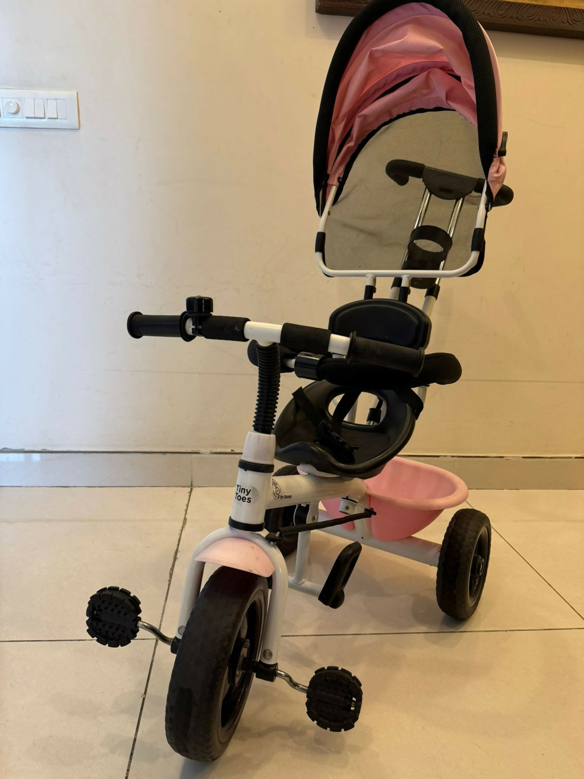 Pink and black tricycle with a mirror on a tiled floor.
