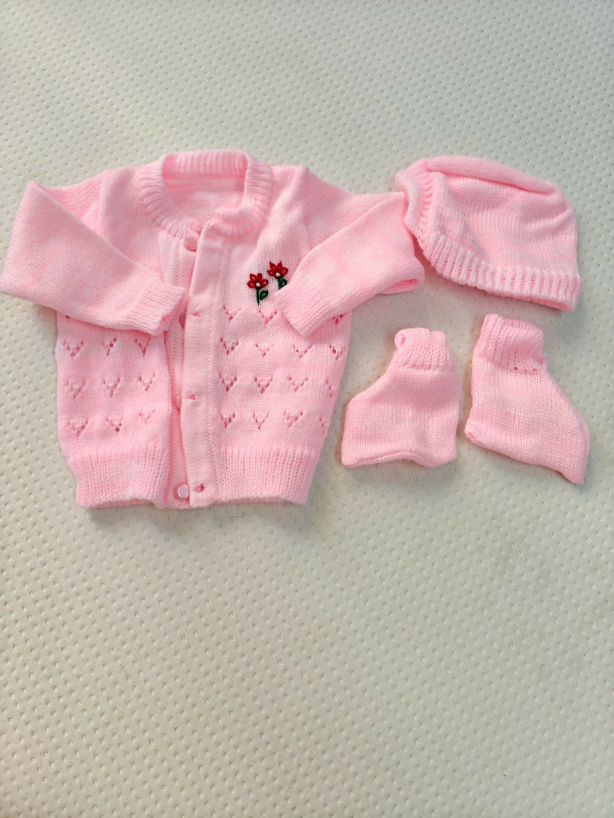Pink baby cardigan, hat, and booties set on a textured surface