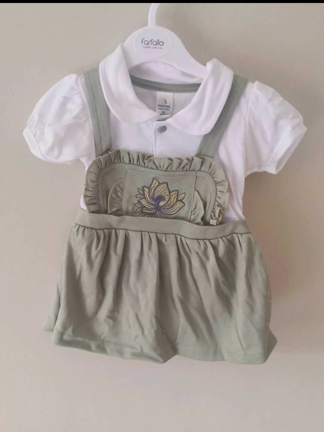 Children's outfit with white shirt and green overalls on a hanger against a beige background