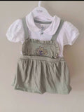 Children's outfit with white shirt and green overalls on a hanger against a beige background