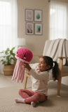 Child holding a pink knitted octopus toy in a room with a plant and chair.