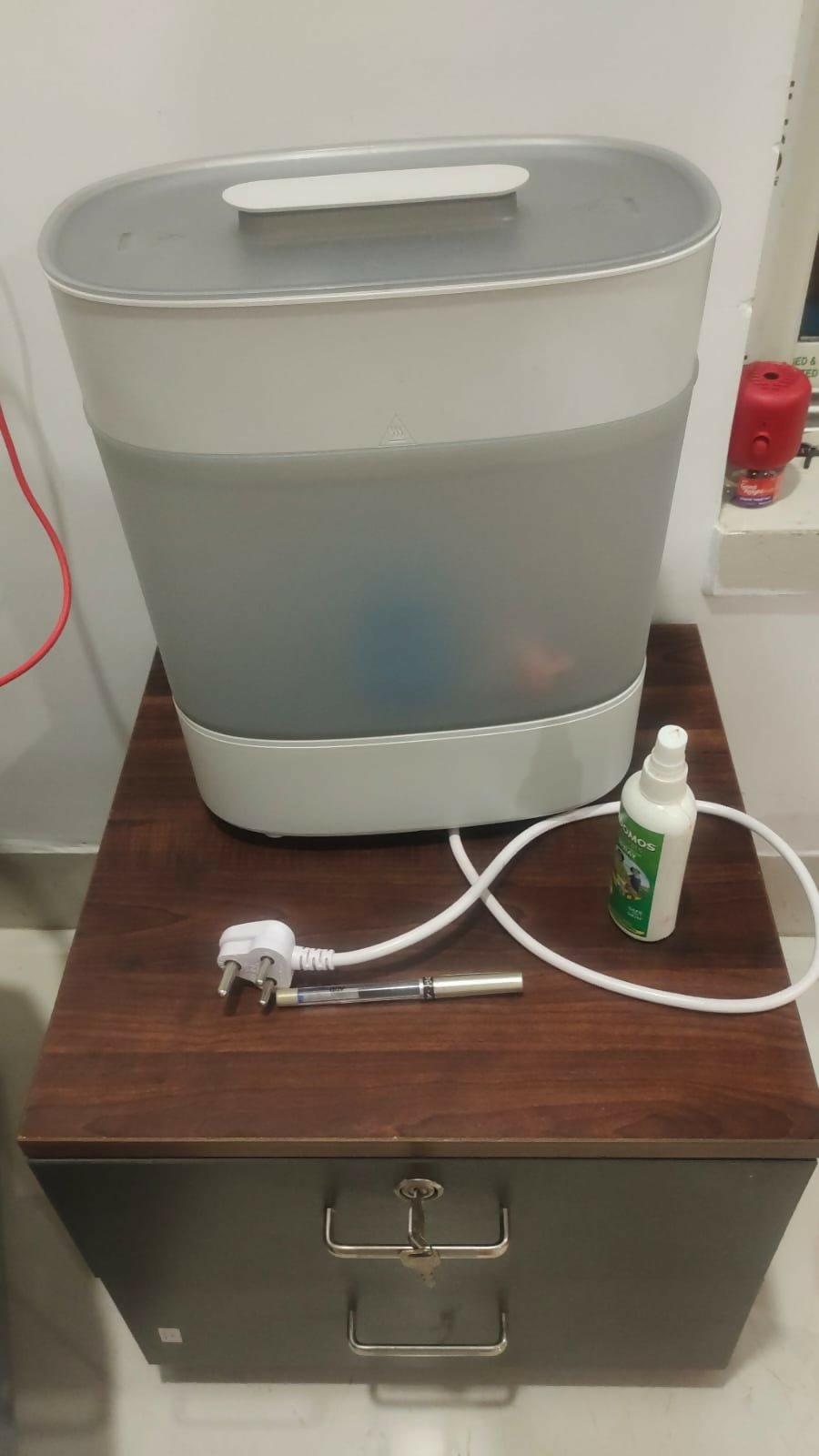 White appliance on a wooden surface with a hose and bottle nearby.