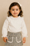 Young girl wearing a white blouse with ruffled details and a patterned skirt