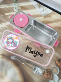 Stainless steel lunch box with pink accents and personalized name on a wooden surface.