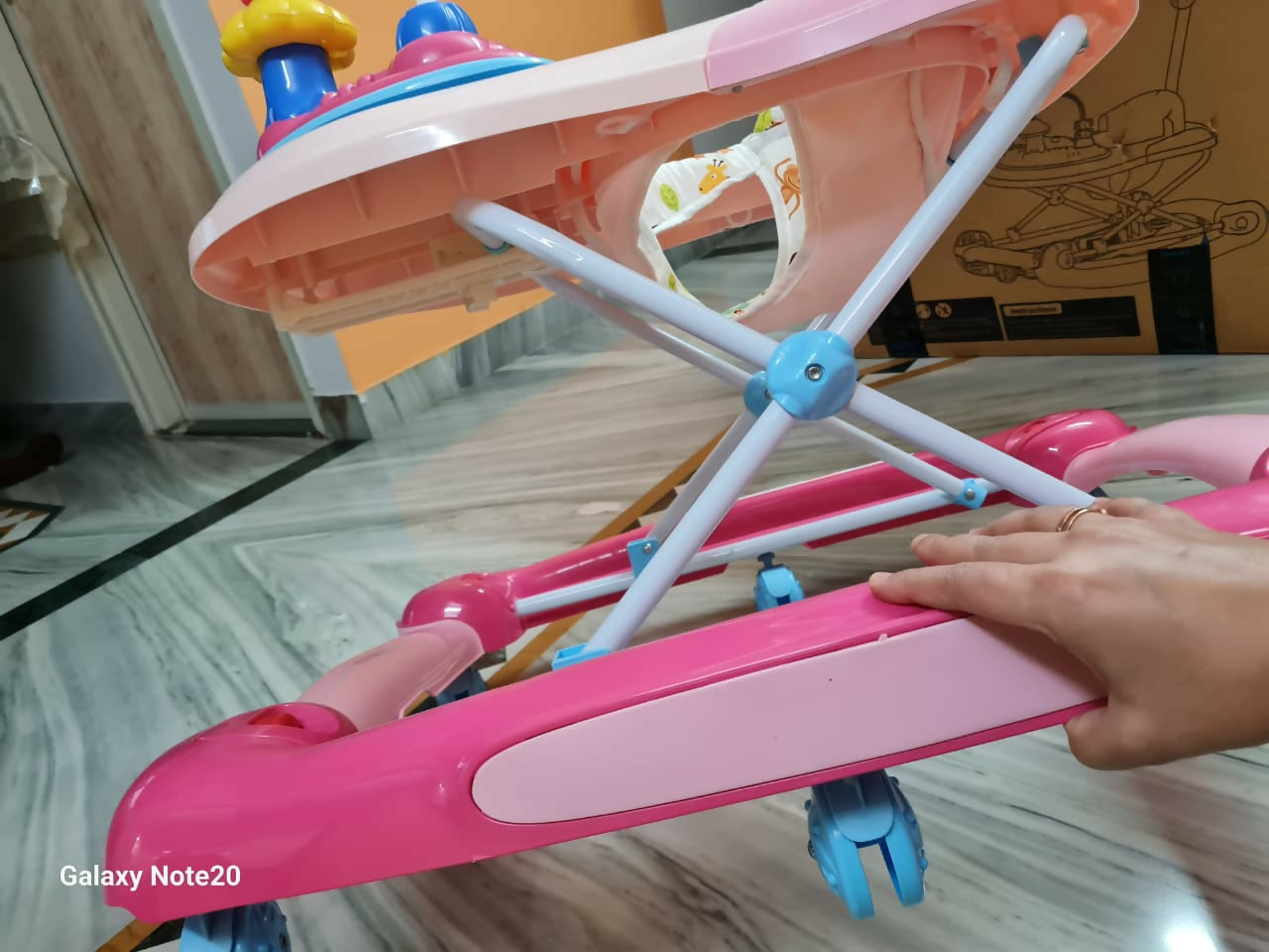Pink and white baby walker on a marble floor with a hand holding it.