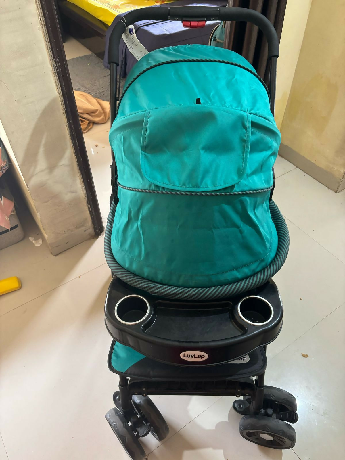 Turquoise stroller with cup holders on a tiled floor