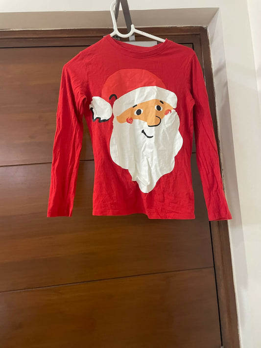 Red long-sleeve shirt with a Santa Claus face design on a wooden surface.