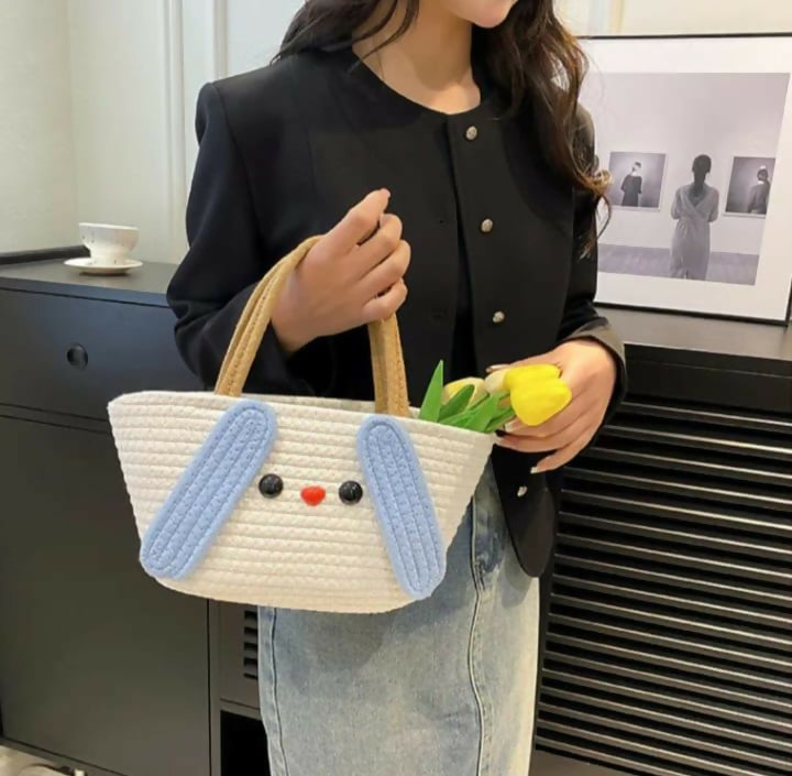 Person holding a white bag with blue bunny ears and a yellow tulip, standing in an indoor setting.