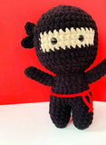 Crocheted ninja toy with a red ribbon against a red background