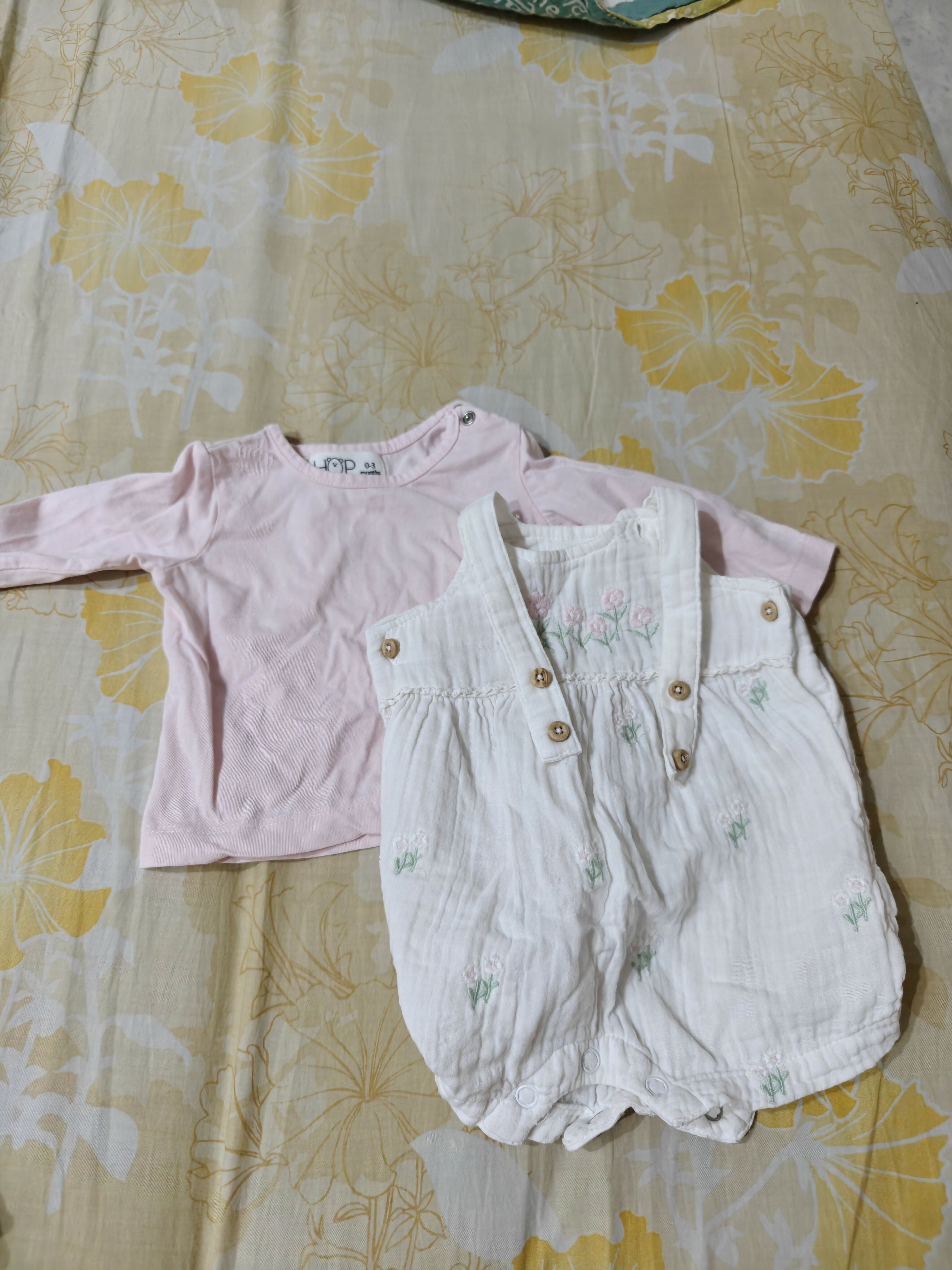 Pink long-sleeve shirt and white overalls on a floral bedspread
