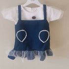 Children's outfit with navy blue dress over white shirt on a hanger against a beige background