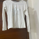 White long-sleeve shirt with a logo on a hanger against a wooden door.