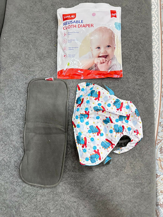 Reusable cloth diaper with pattern, gray pouch, and Luvlap brand packaging on a gray surface.