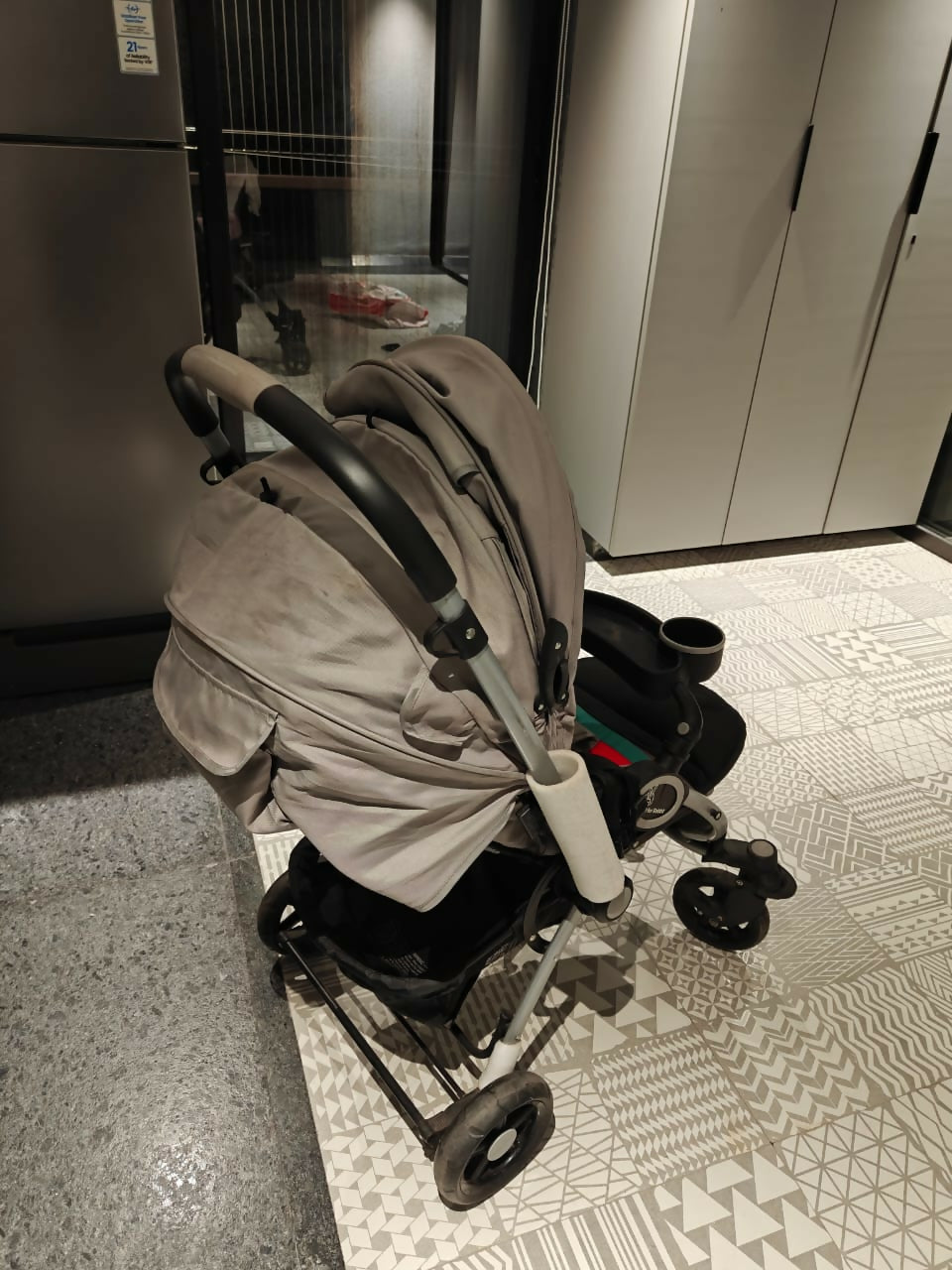 Beige stroller on a patterned floor next to a glass door