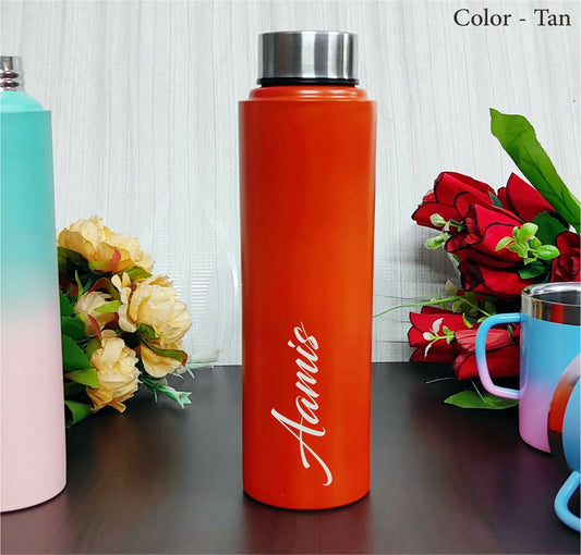Orange water bottle with 'Aamus' branding on a wooden surface with flowers and other items.