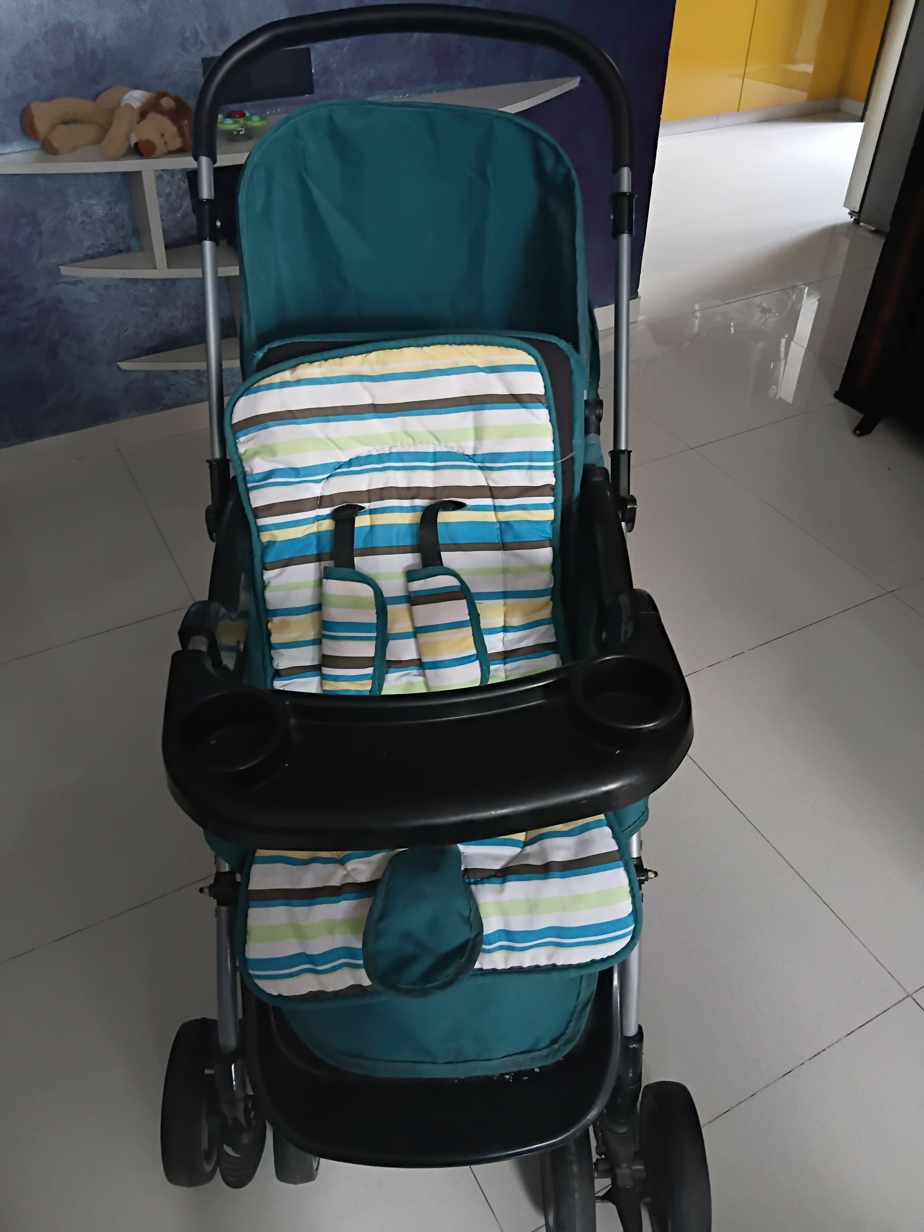 Blue baby stroller with a striped cover on a tiled floor.