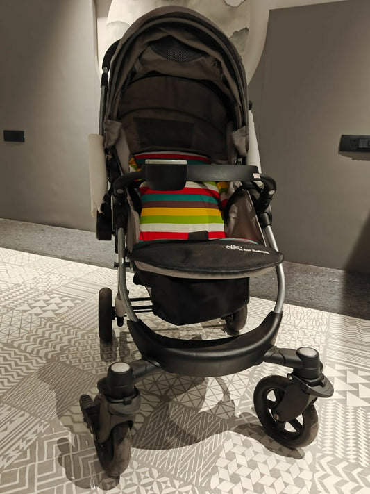Black stroller with a colorful striped bag on a patterned floor.