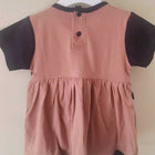 Pink dress with black sleeves and trim on a hanger against a beige background
