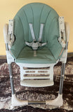 Green baby high chair with straps on a marble surface