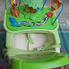 Green baby swing with colorful animals and toys on a checkered floor.