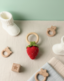 Strawberry-shaped teething ring with wooden rings and baby booties on a light surface.