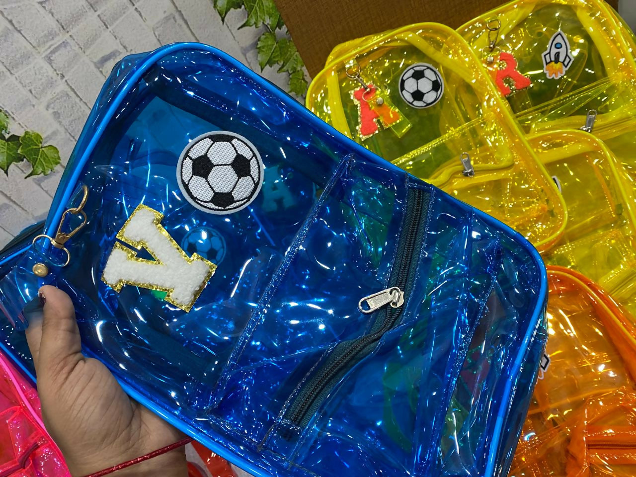 Blue transparent pouch with soccer ball design held by a hand, surrounded by other colorful pouches.