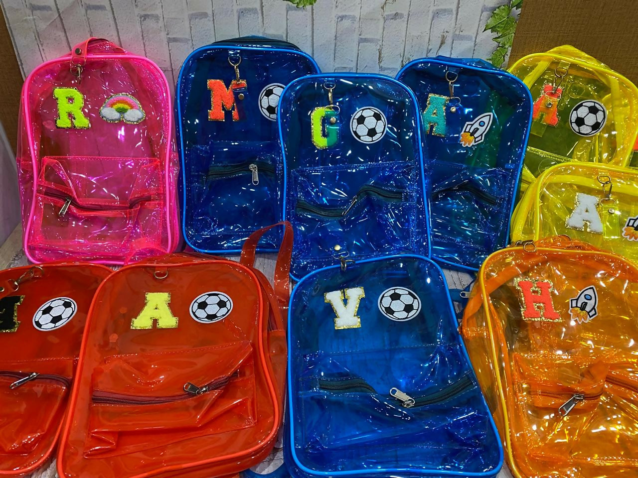 Colorful transparent backpacks with letters and sports ball designs on a white background