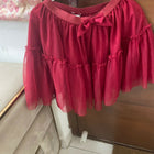 Red blouse with ruffled sleeves and a bow on a hanger against a wooden door.