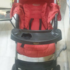 Red stroller with a black tray on a marble floor.