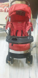 Red stroller with a black tray on a marble floor.