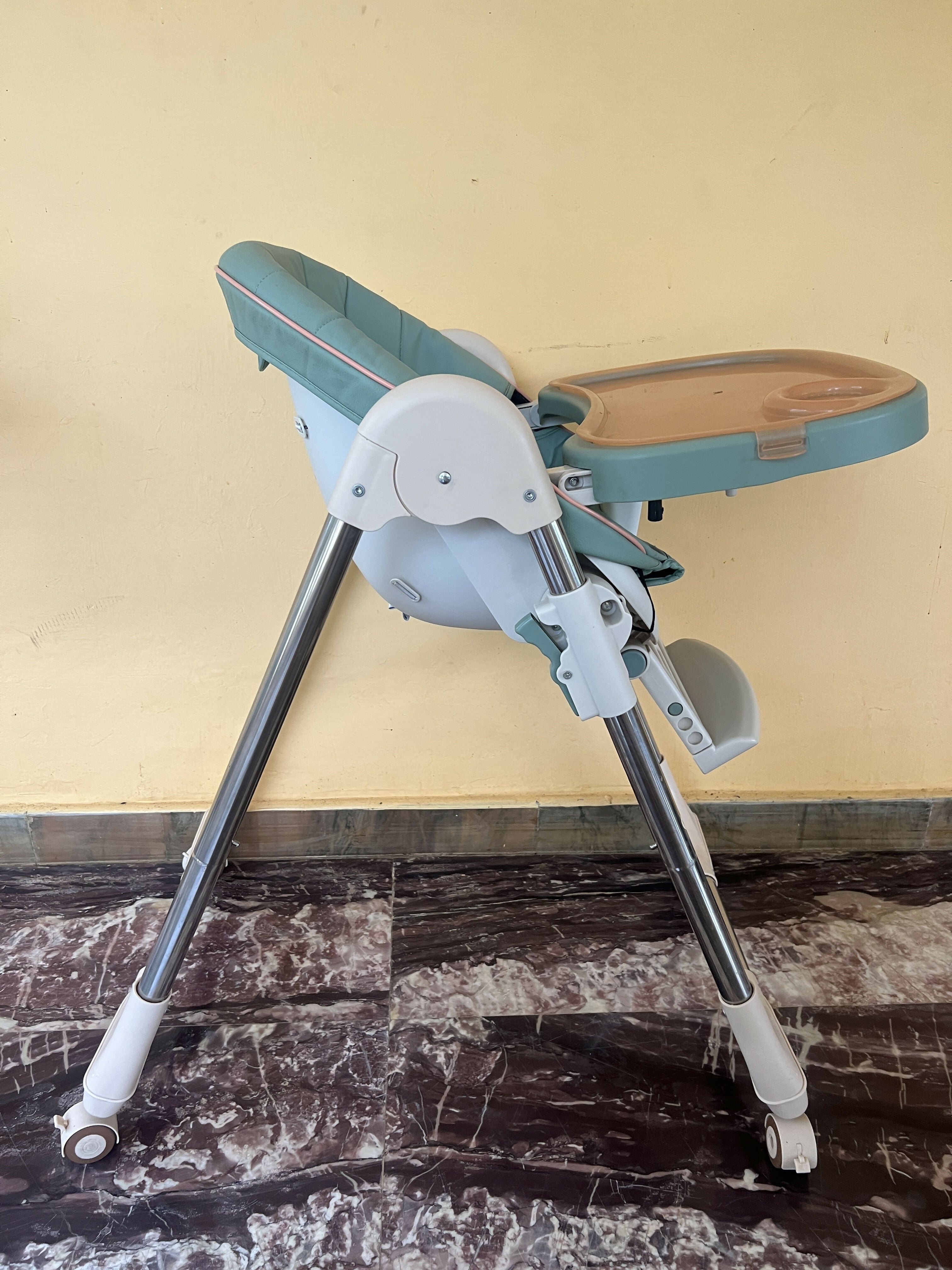 Foldable high chair on a marble floor with a yellow wall background