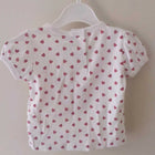 White baby shirt with pink heart pattern on a hanger against a white wall