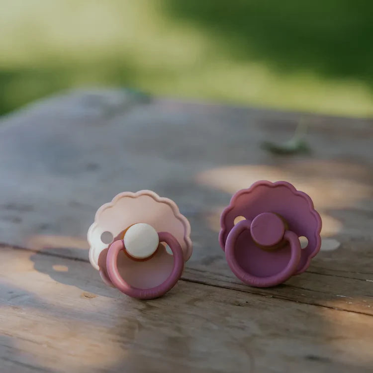 Two pink pacifiers on a wooden surface with a blurred green background