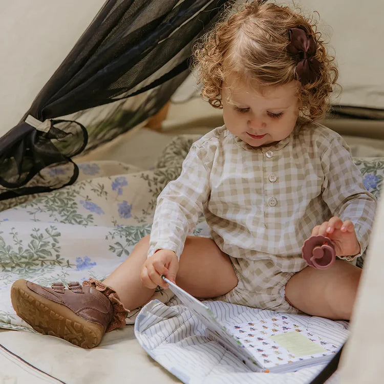 Child sitting on a bed reading a book with a pacifier in hand