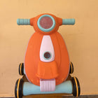 Orange toy scooter with blue handlebars on a wooden surface against a beige wall.
