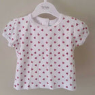 White baby shirt with pink heart pattern on a hanger against a beige wall.