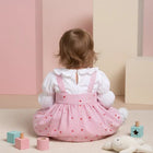 Child wearing a pink dress with white ruffled shirt