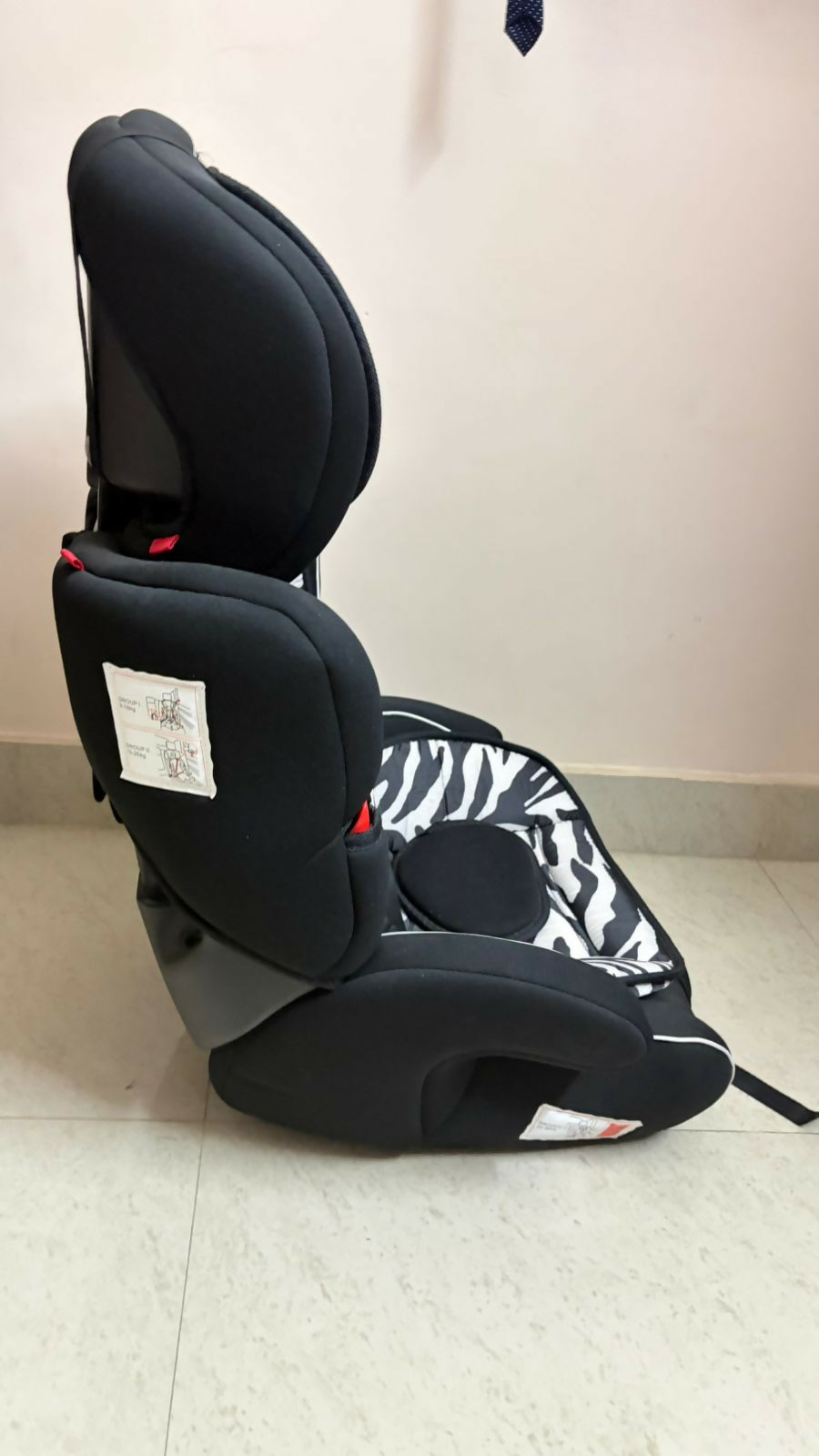 Black and gray car seat with zebra pattern on a light-colored floor.