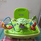 Green baby activity center with colorful toys on a checkered blanket.