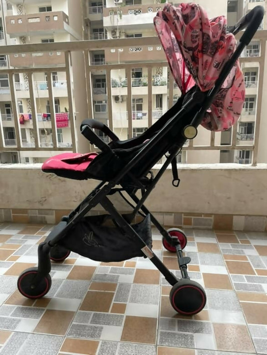 Black and pink stroller on a tiled floor with buildings in the background