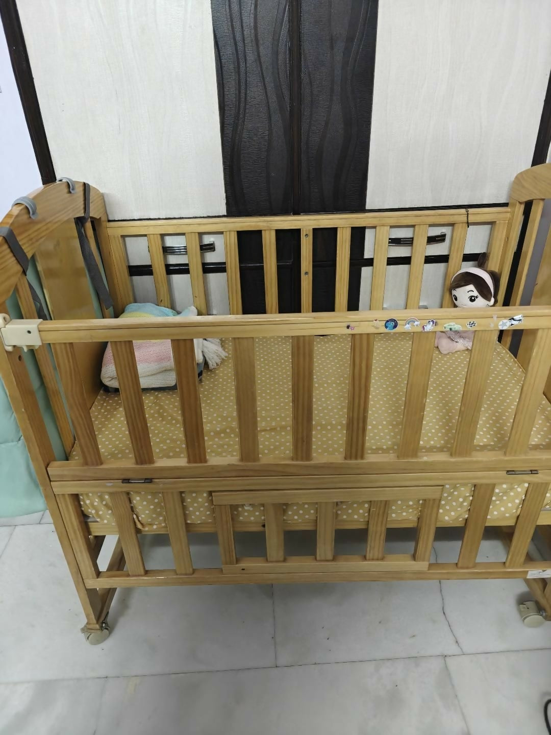 Wooden crib with wheels on a tiled floor against a striped wall.