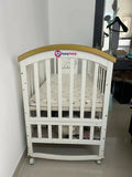 Shop Huny Huny Convertible Baby Cot – Wooden crib with storage, teething rails, wheels, and adjustable height.